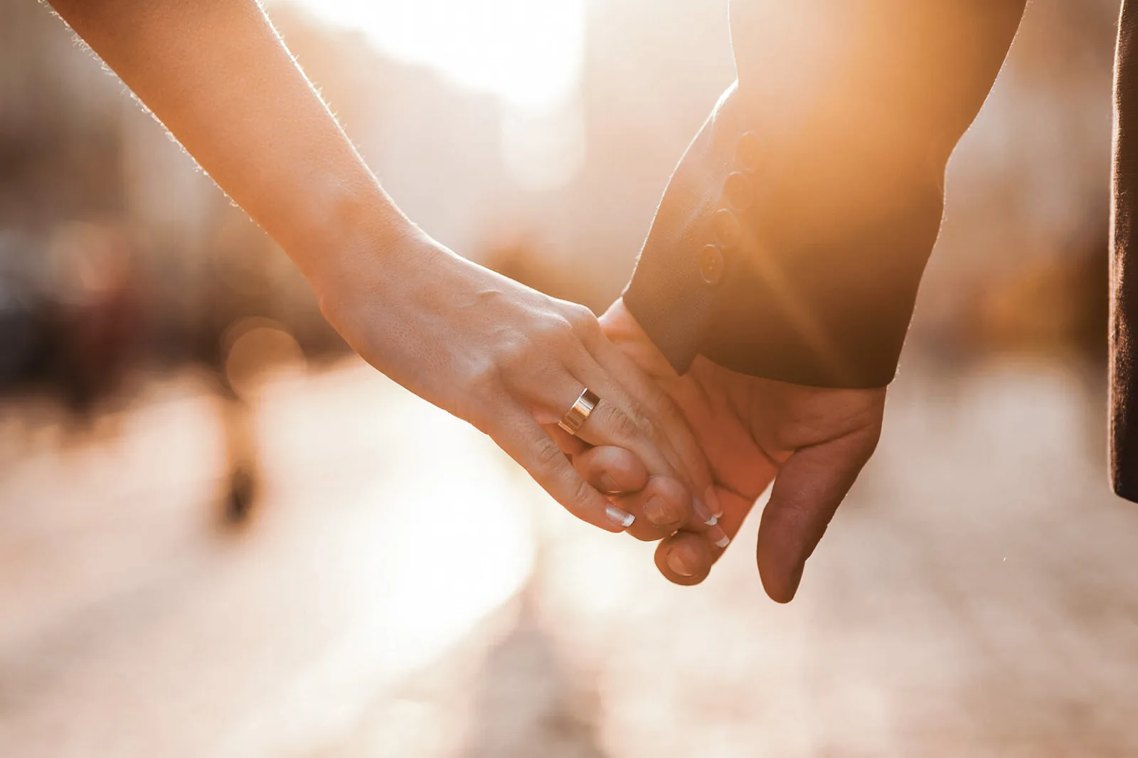 A married couple holding hands at sunset, one wearing a wedding ring